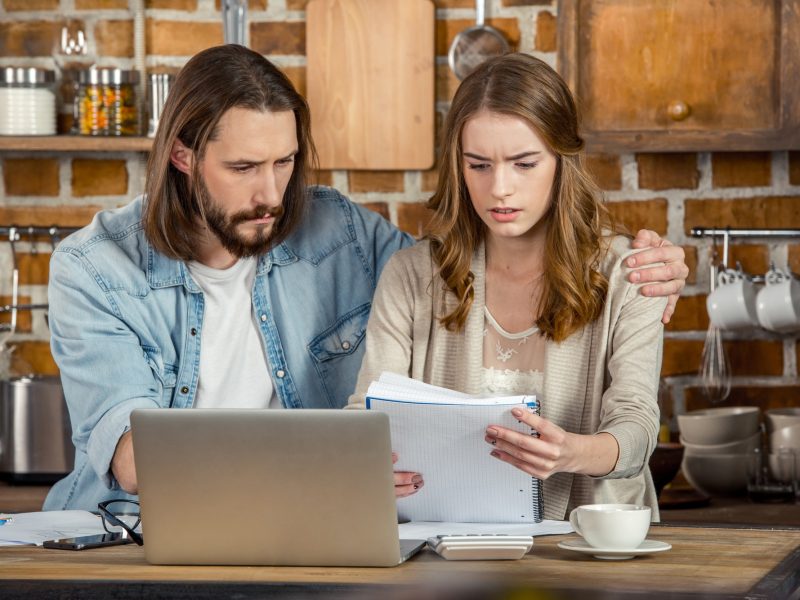 Upset young couple looking at documents while working in home office